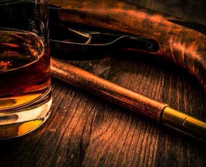 Verre de whisky et fusil sur bois sombre, ambiance années 1920 chez Aventure Live! Escape Game