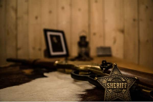 Badge Sheriff en métal près d'une carabine, décor de bois, salle Evasion au Far-West chez Secret Room