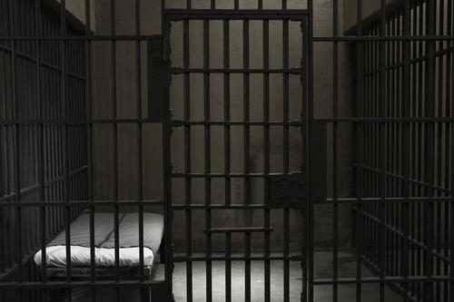 Cellule de prison aux barreaux noirs avec un lit au matelas blanc, salle Piégés chez Escape Yourself à La Rochelle