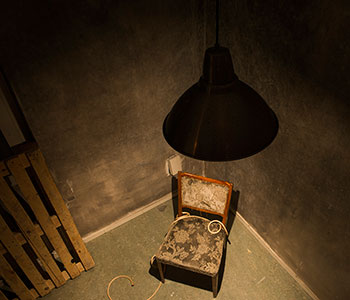 Chaise capitonnée dans un coin sous une lampe suspendue, palettes en bois, salle Le tueur du Zodiac chez Fox in a Box au Cannet