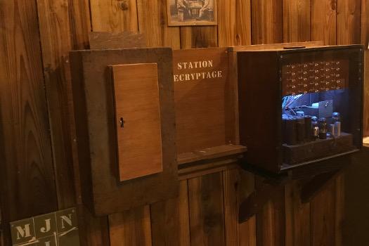Meuble en bois étiqueté Station décryptage avec trappe et boîtier lumineux, salle 1916 chez La Clé du Bastion