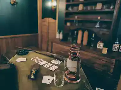 Table de saloon avec cartes à jouer, lanterne et verre, étagère de bouteilles au fond, salle Braquage au Far West chez Les Frères Pillard