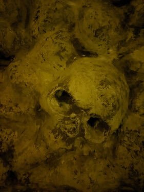 Crâne et ossements dans une lueur jaune sombre, salle Les souterrains de Richelieu à Sainte-Gemme-la-Plaine