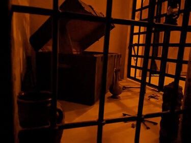 Porte à barreaux et escalier dans une lueur orangée, salle Les souterrains de Richelieu chez La Boîte à CL-é