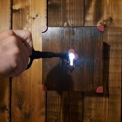 Main tournant une clé dans une serrure lumineuse sur un panneau de bois, salle L'héritage de tante Suzanne chez Zone 72