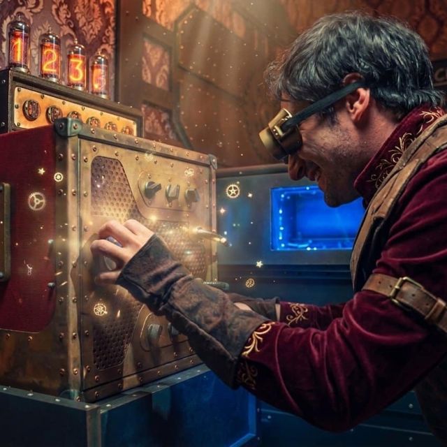 Joueur à lunettes de soudeur réglant une machine à voyants dans un décor tapissé, salle Steampunk chez BlackOut Room