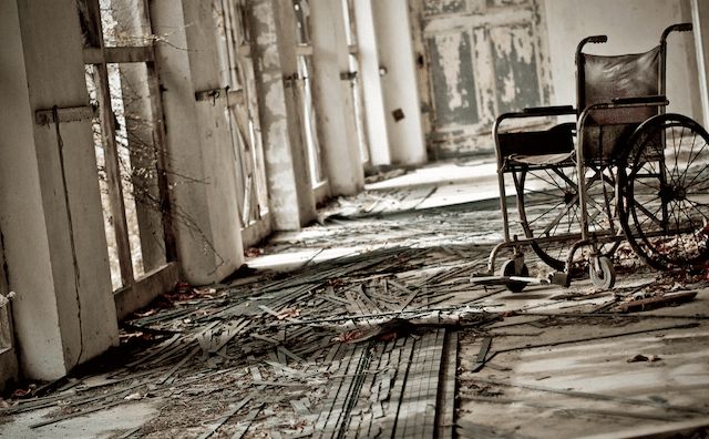 Couloir délabré d'asile avec fauteuil roulant abandonné et murs décrépit