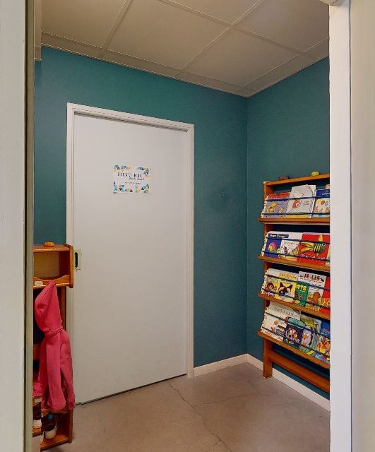 Pièce aux murs turquoise avec porte blanche, rayonnage de magazines colorés, décoration enfantine chez La Synapserie