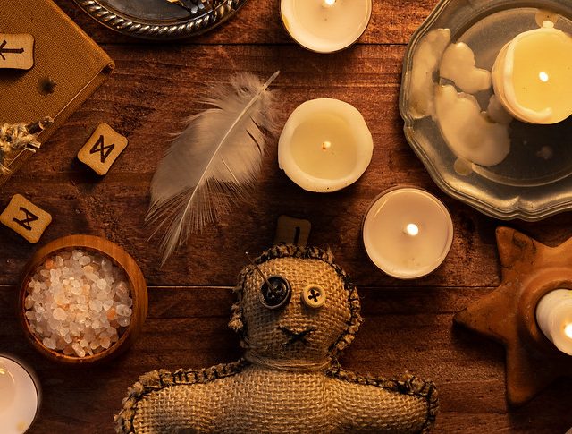 Bougies, plume, poupée vaudou et lettres de bois sur une table, salle Le secret de la voyante chez Alive Room à Bayonne