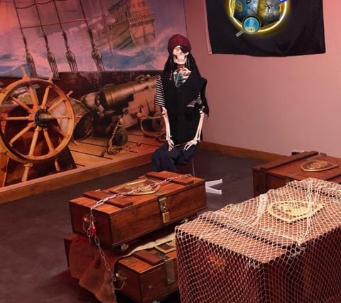 Squelette de pirate assis parmi des coffres en bois, affiche de l'escape box Le trésor perdu des 4 Pirates