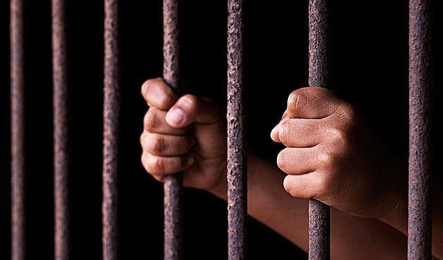Mains agrippant les barreaux rouillés d'une cellule de prison, atmosphère carcérale sombre