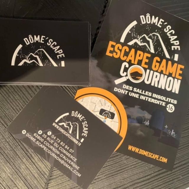 Cartes de visite Dôme'scape et flyer Escape game Cournon posés sur une table sombre, enseigne de Cournon-d'Auvergne