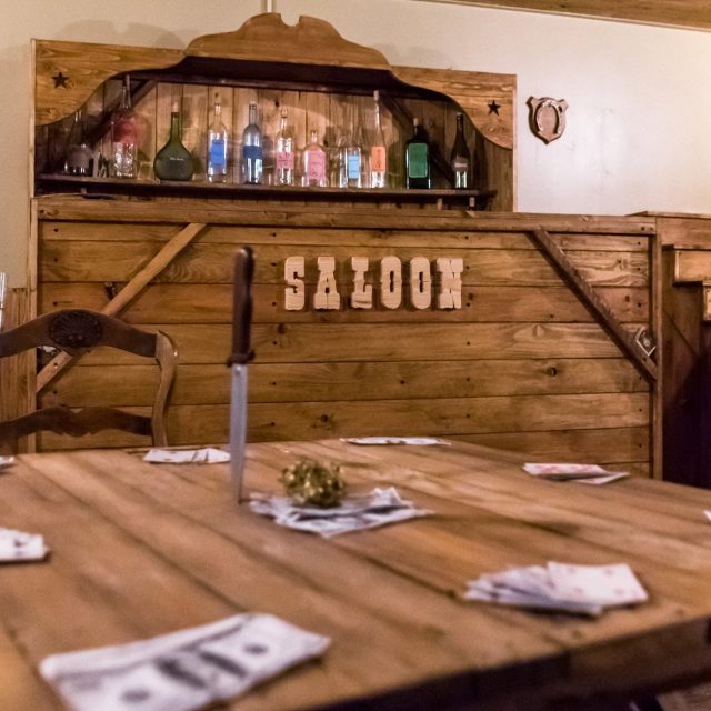 Décor de saloon en bois avec comptoir, bouteilles et accessoires Western chez Escape : The Movie à Marseille