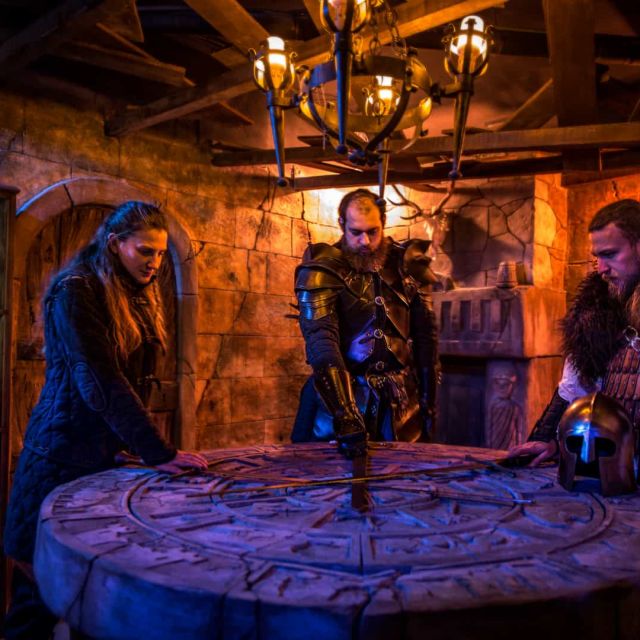 Quatre joueurs autour d'une table ronde dans un décor médiéval aux teintes orange et bleues, à La malédiction de Morgane