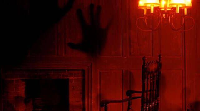 Décor rouge sang avec néon, main à la fenêtre, escalier sombre chez Intrappola
