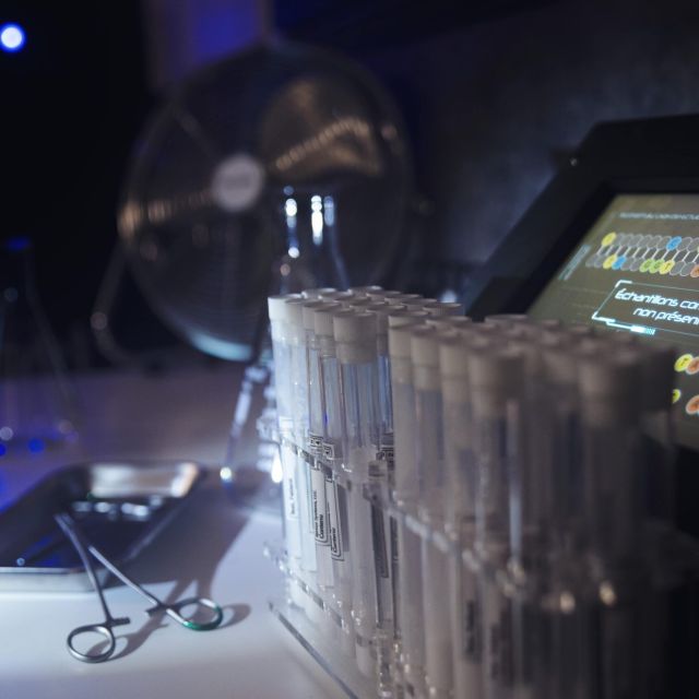 Rack de tubes à essai et tablette lumineuse dans un laboratoire sombre, salle L'experience Interdite chez Hint Hunt