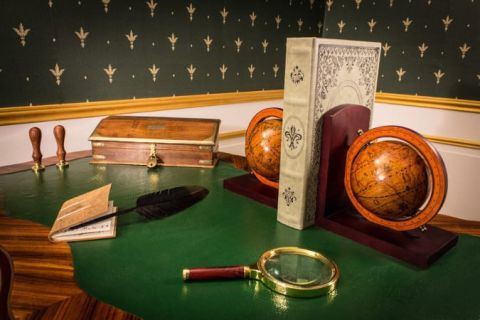 Décor XIXe siècle avec globes terrestres, livres, loupe et objets scientifiques sur table verte dans Le secret de Nicéphore Niépce