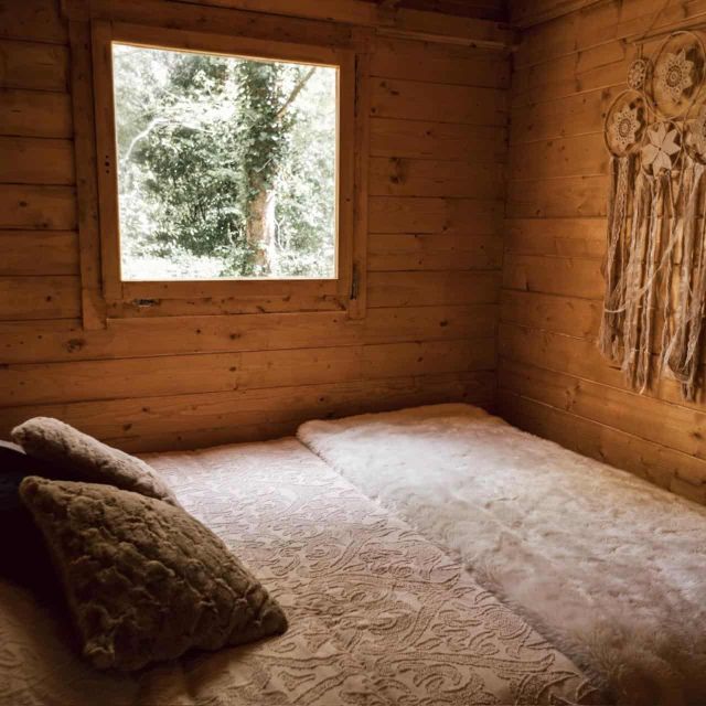 Chambre de cabane en bois avec matelas, coussins et attrape-rêves, salle Cabane Yavana chez L'Escale des Elfes