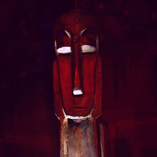 Masque moaï rouge aux yeux luminescents sur fond sombre, chez Imaginarium Game à Lyon
