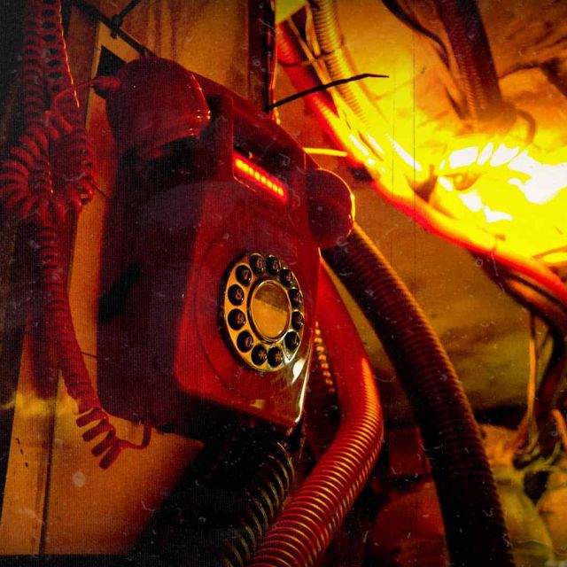 Téléphone rouge à cadran branché sur un tuyau orange éclairé de jaune, salle Carbon Copy chez Prizoners à Saint-Pierre