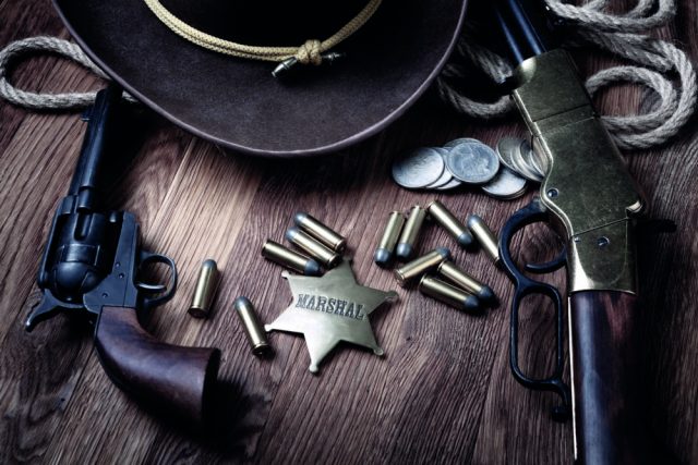 Revolver, balles, étoile Marshal et pièces posés sur une table avec un chapeau de cow-boy, visuel de LockedUp à Lieusaint