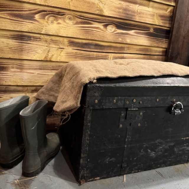 Malle noire recouverte de toile de jute et bottes en caoutchouc, salle Le secret du paludier chez Escape Factory à Guérande