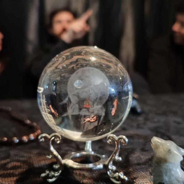 Boule de cristal sur une table drapée, perles et petite figurine, spectateurs flous derrière, salle Loup Garou chez Goodlock à Bordeaux
