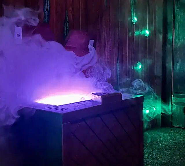 Coffre fumant éclairé de violet dans une cabane en bois, salle Malédiction chez Evade