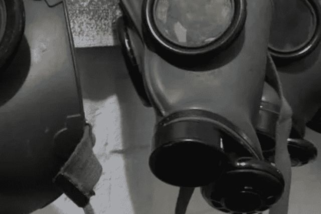 Rangée de masques à gaz noirs en noir et blanc, salle Contamination chez Escape Yourself au Mans