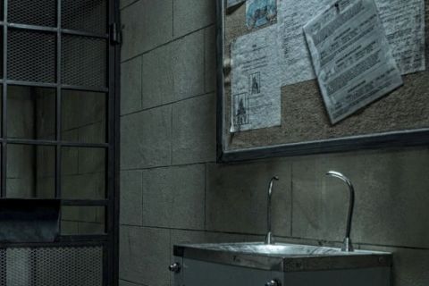 Cellule carcérale austère avec lavabo métallique, documents affichés et porte grillagée dans Prison Break