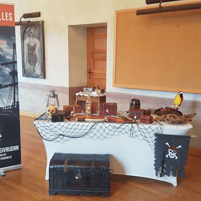Table couverte d'un filet, coffres et perroquet devant une affiche Escape Game Crolles