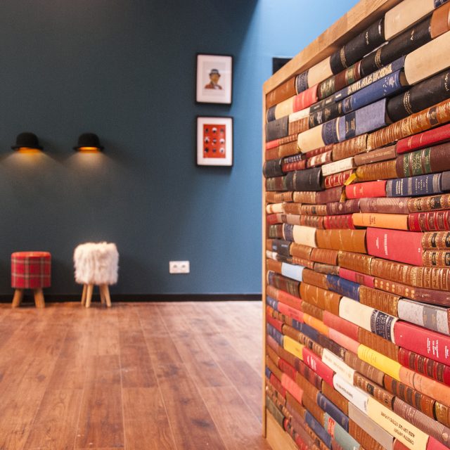 Salle d'attente bleu canard avec poufs et mur de reliures de livres, enseigne Lock Academy à Toulouse