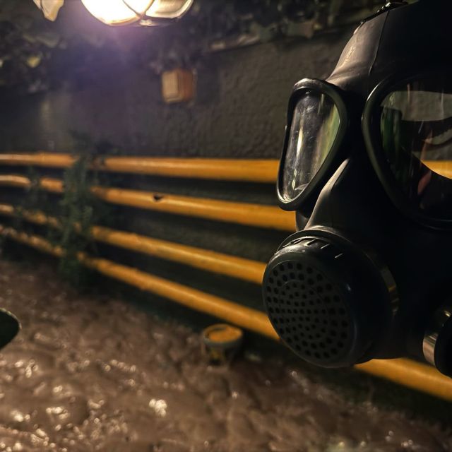 Masque à gaz devant des tuyaux jaunes dans un couloir sombre, salle Explosion à Biotech chez Time Lapse