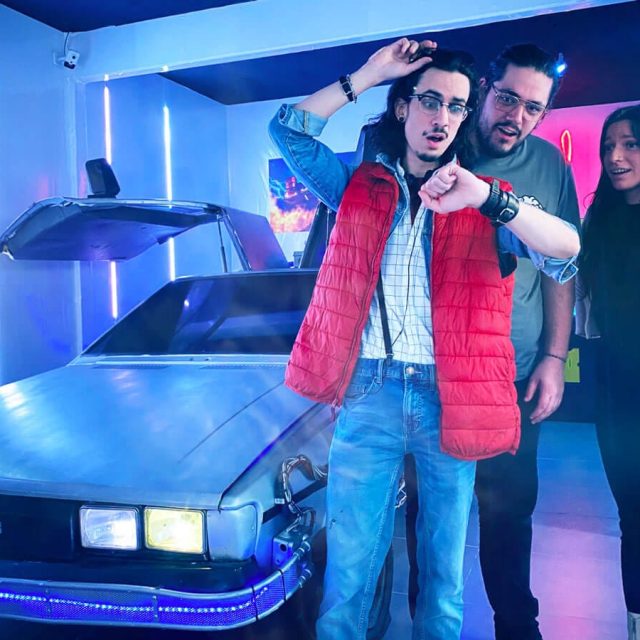 Trois joueurs devant une voiture futuriste, l'un en gilet rouge regardant sa montre, salle Retour dans le temps chez Freeing