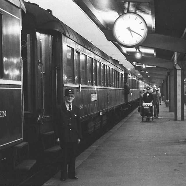 Quai de gare avec train, horloge, porteur en uniforme, voyageurs chez 221B Baker Street à Dijon