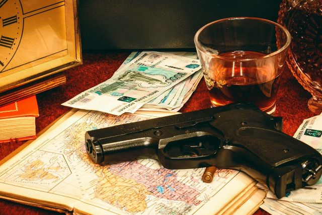Pistolet posé sur une carte, liasses de billets, verre et réveil, salle Opération Sibéria chez Team Quest à Montélimar