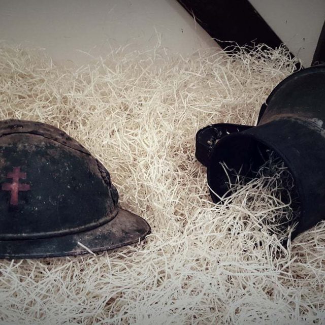 Casque militaire à croix rouge et obus sur lit de paille, décor de tranchées chez Enigm antic