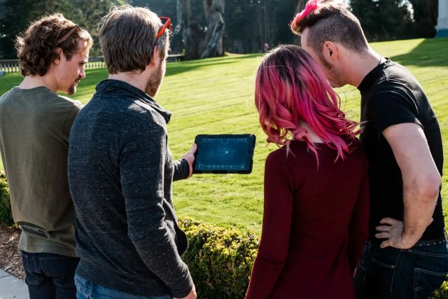 Quatre joueurs en plein air regardant une tablette tactile sur une pelouse, salle Opération Mindfall à Deauville