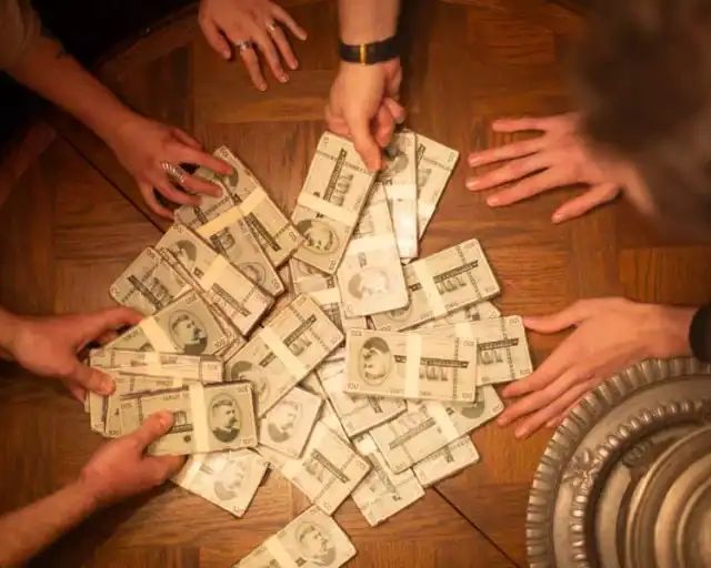 Mains de joueurs triant des liasses de billets sur une table en bois, salle La fortune du fondateur chez Gaillard Académie