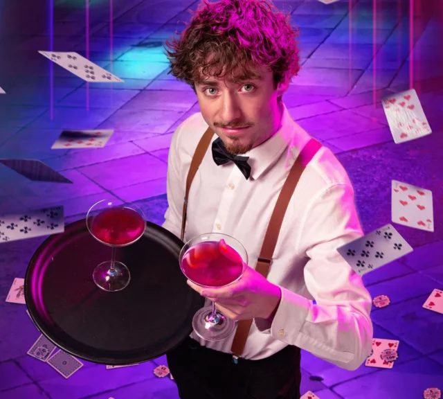 Homme en gilet et nœud papillon portant un plateau de verres rouges, cartes qui volent, salle Les secrets du Flamingo, Under Escape