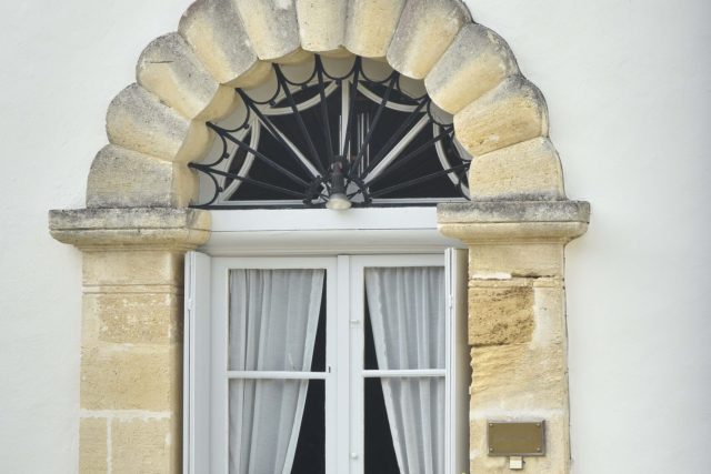 Porte-fenêtre blanche à voilages surmontée d'une arcade de pierre en coquille, Château de Lisennes à Tresses