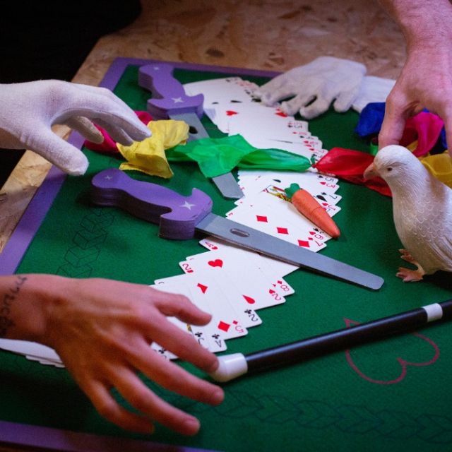 Mains gantées sur un tapis vert avec cartes, colombe blanche, foulards et baguette, salle La Grande Illusion à Metz