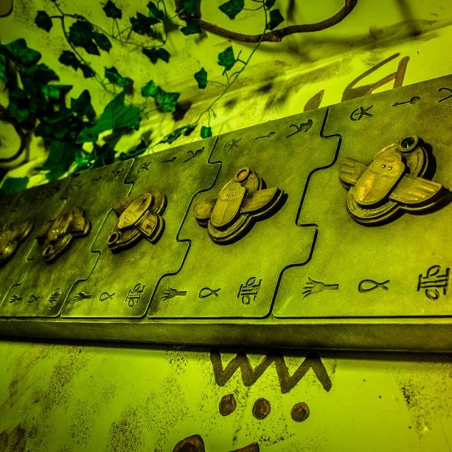 Plaque gravée avec hiéroglyphes et figurines dorées sous éclairage vert, au Tombeau perdu