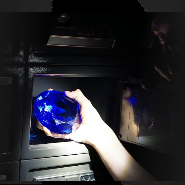 Main tenant un objet bleu luminescent devant un écran dans Braquage de la banque évolutive