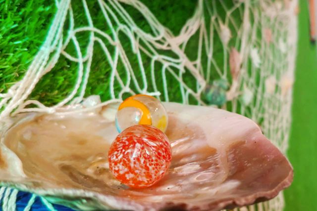 Coquille nacrée portant une bille de verre orange sur un filet et du gazon, salle Au pays des merveilles chez Locked Time