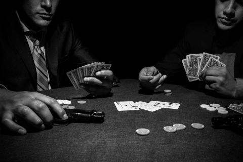 Deux hommes en costume autour d'une table de jeu, cartes et jetons, ambiance clandestine chez Mamma Mafia à Strasbourg