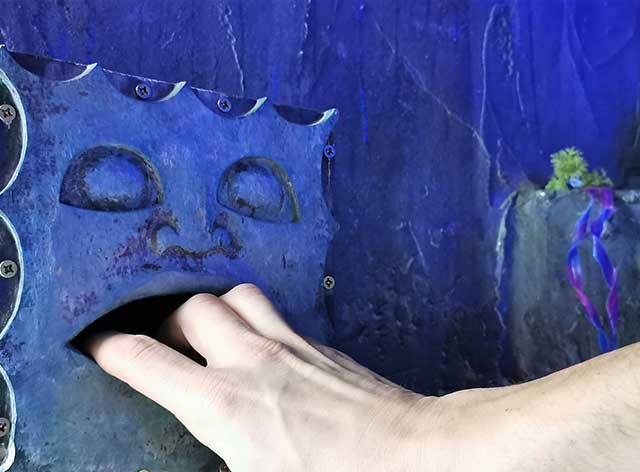Main posée sur un mécanisme bleu rouillé, décor aquatique souterrain d'Atlantis : l'île secrète
