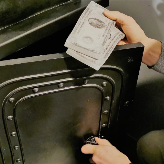 Main sortant des billets d'un coffre-fort métallique vert, salle Comics City chez Captive Live Escape Game à Clichy