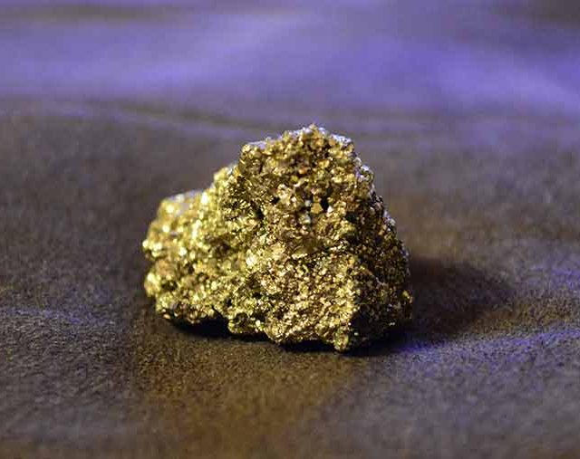 Pépite d'or brute posée sur du sable sous une lumière violette, salle La ruée vers l'or chez Time Lapse