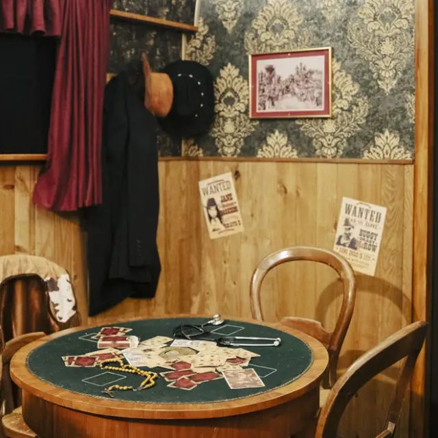Table de jeu verte entourée de chaises, porte à barreaux noire, salle Le Silver Express chez Escape Time à Pertuis